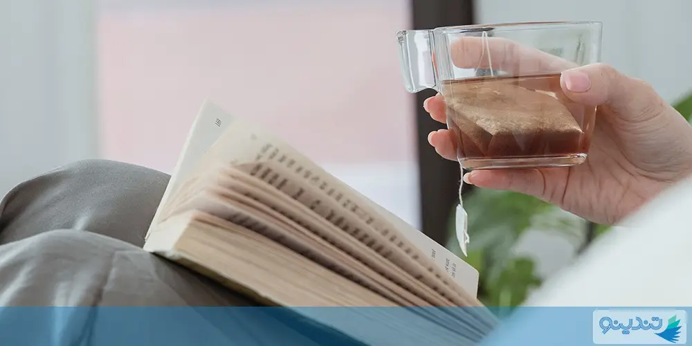 نمای نزدیک کتاب در حال مطالعه کنار یک لیوان چای
